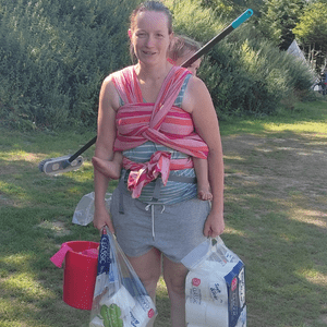 Frau mit Kind auf dem Rücken und mit Putzeimer und Lappen in der Hand.