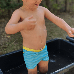 Ein Kleinkind badet mit Badehose in einem kleinen Zuber